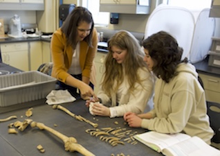 Two students examine bones while their instructor coaches them.
