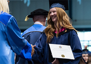 Brielle Pedersen Skene walks across the convocation stage in cap and gown holding her degree